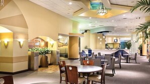 A spacious hotel lobby with multiple seating areas, a reception desk, and a staircase leading to upper floors.