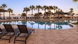 A poolside area with lounge chairs and umbrellas, palm trees, and a view of the ocean.