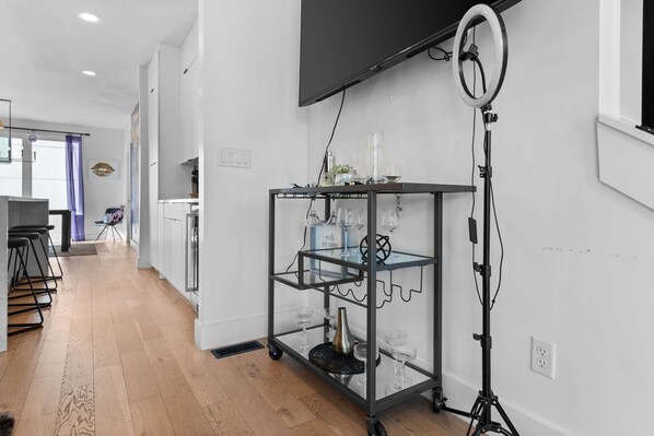 A modern kitchen with a wooden floor, a glass cart with kitchenware, and a ring light on a tripod.