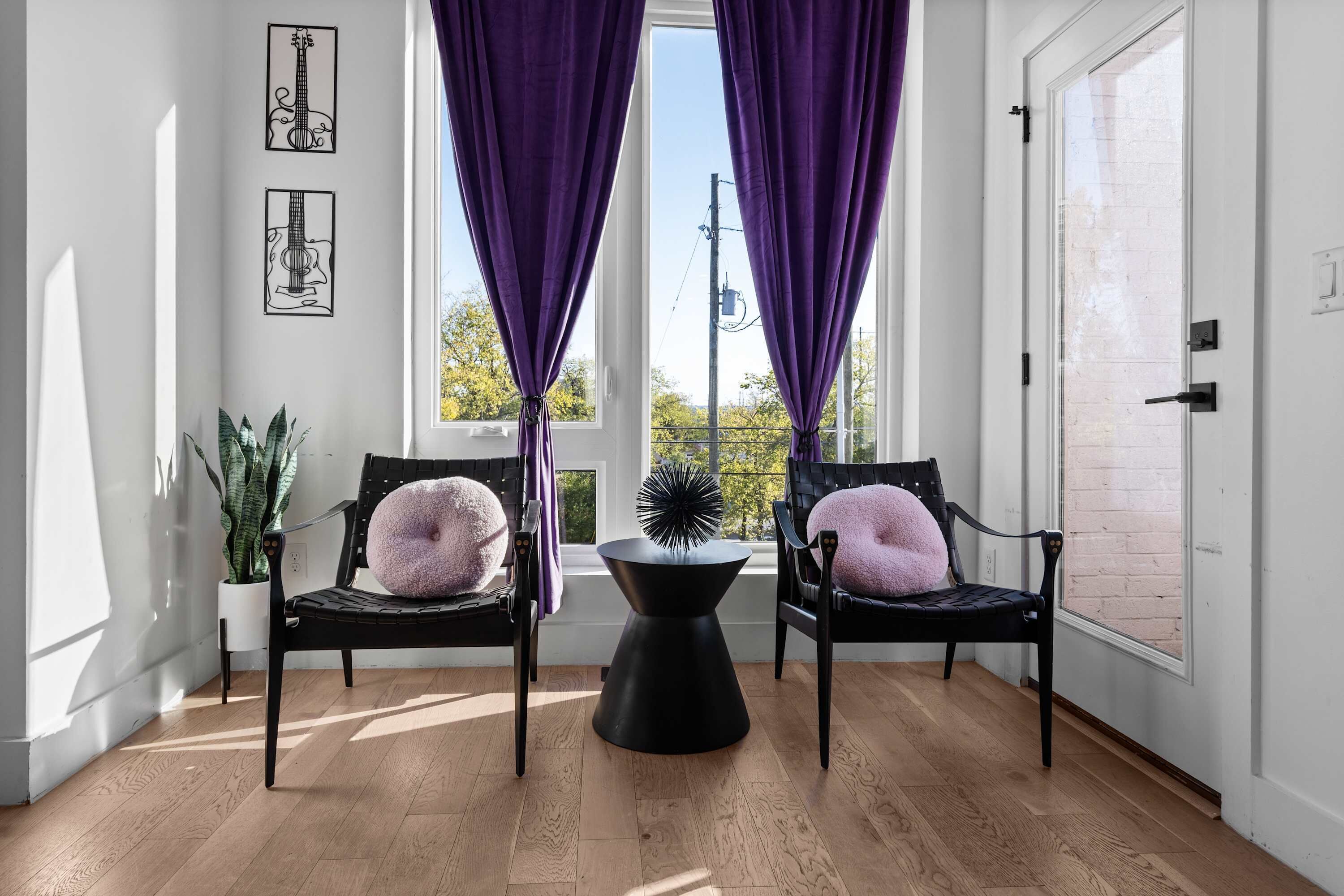 A room with two black chairs, a black table, purple curtains, and framed artwork on the wall.