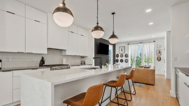 A modern kitchen with a large island, bar stools, pendant lighting, and a view of the outdoors. - Group-Friendly 2 Nashville Homes • Sleeps 15 (Nashville)