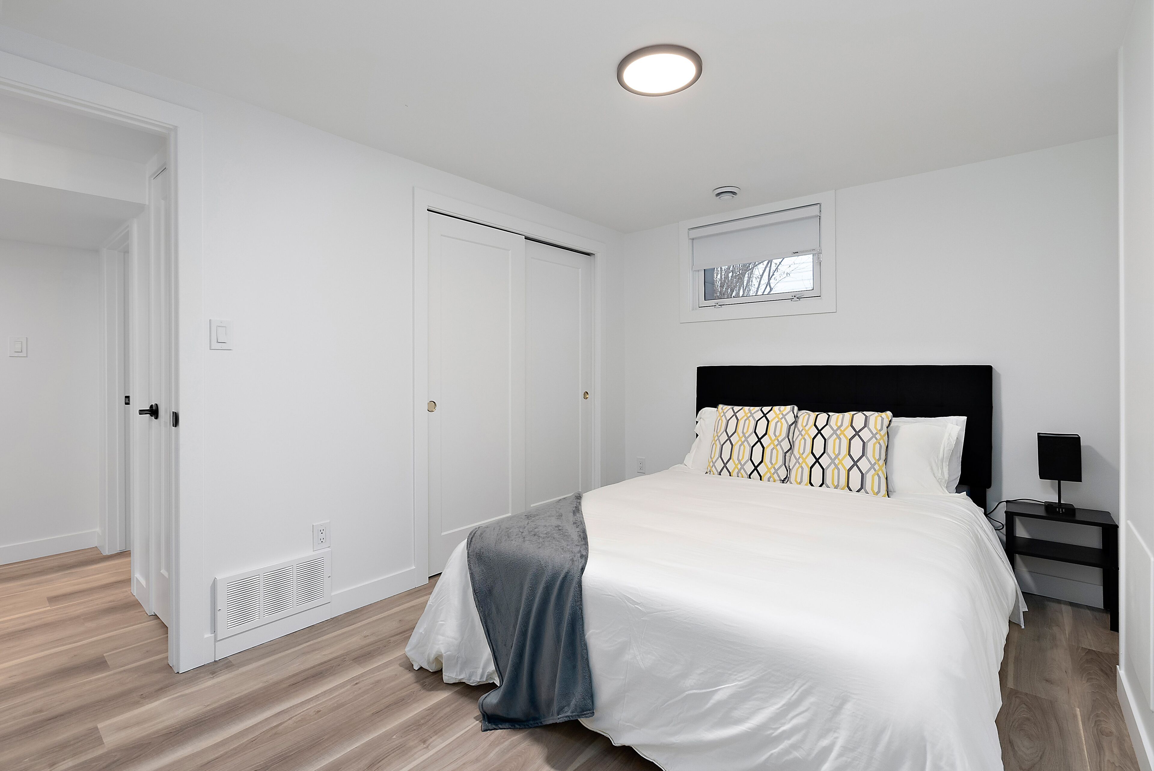 A bedroom with a bed, a nightstand, a window, and a door.