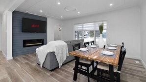 En moderne stue med en grå sofa, et træspisebord dækket til fire personer, og et fladskærms-tv ophængt på væggen.