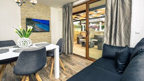 A modern living room with a dining area, featuring a sofa, dining table, chairs, and a TV mounted on a brick wall.