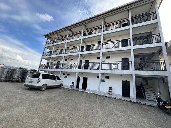 Un edificio de varios pisos con balcones, una camioneta blanca y una motocicleta estacionadas al frente.