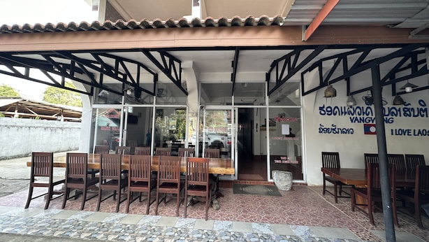 An outdoor seating area with wooden tables and chairs, a tiled floor, and a sign for SANTI VILLA. - VangVieng Santara Hotel (Vang Vieng)