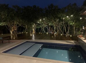 A swimming pool with a tiled edge, surrounded by trees and illuminated by string lights.