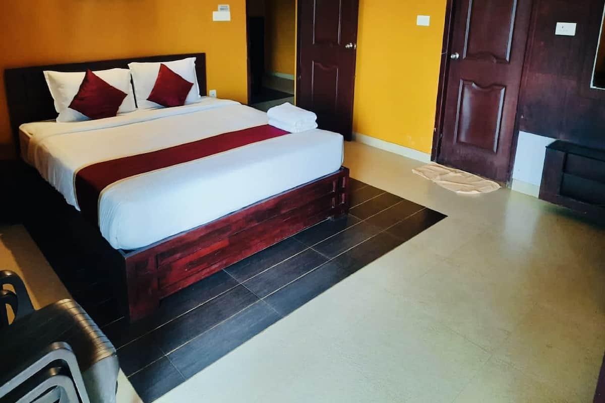 A hotel room with a large bed, two doors, a framed picture on the wall, and a small table with a chair.