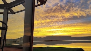 A sunset over a calm lake with mountains in the background, viewed through a glass structure. - Titicaca Los Uros vanalux (Puno)