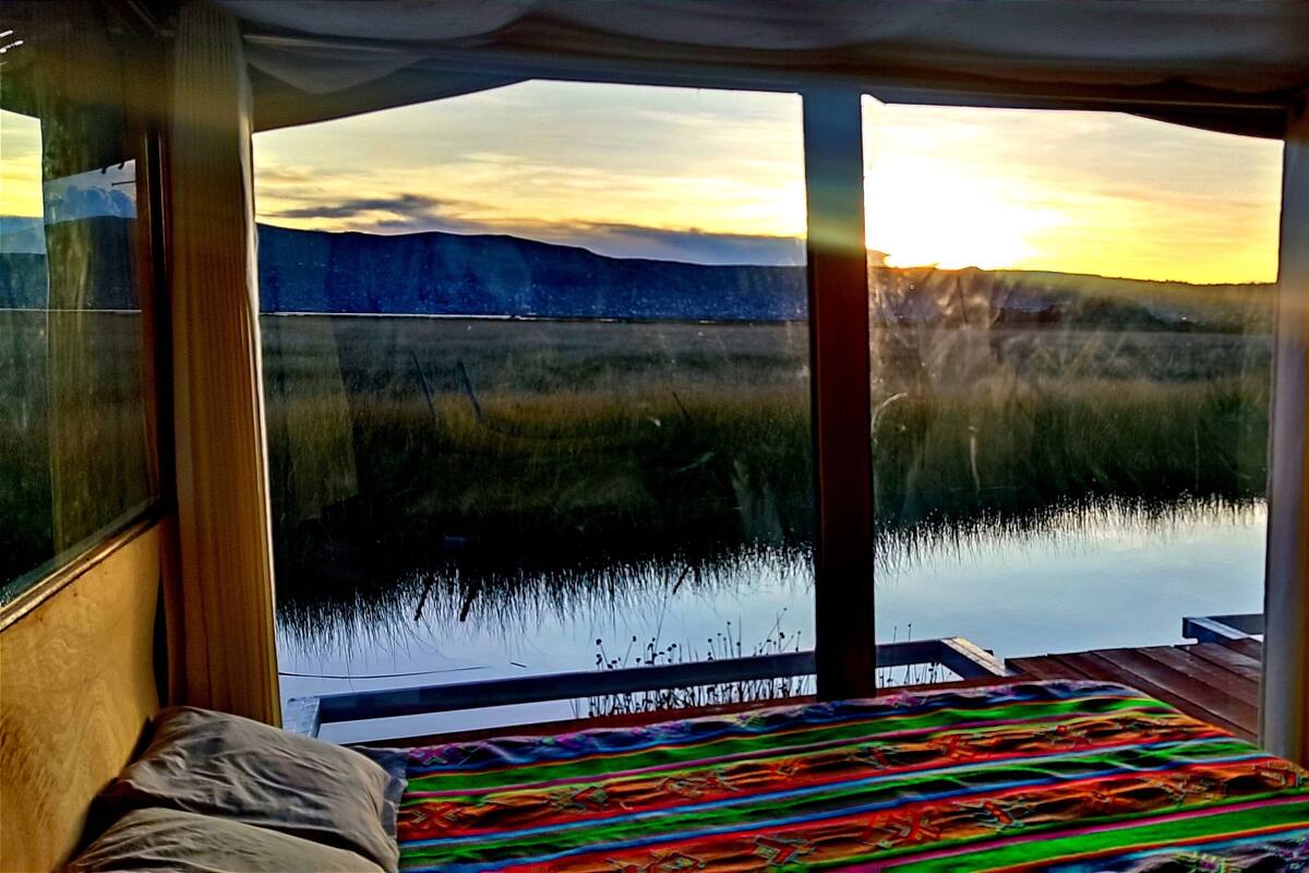 Une chambre avec un lit, une vue sur un lac et un coucher de soleil.