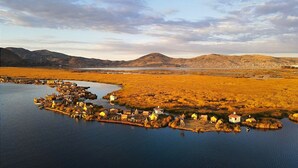 A lakeside village with houses built on stilts, surrounded by a flat landscape and mountains in the distance. - Titicaca Los Uros vanalux (Puno)