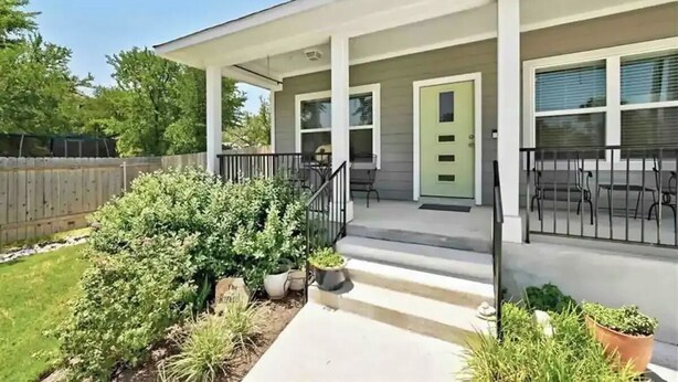 Een woonhuis met een overdekte veranda, een voordeur en een kleine tuin.
