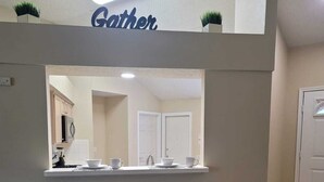 Et lille tekøkken med to sorte barstole, en bordplade og et skilt med teksten "Gather".