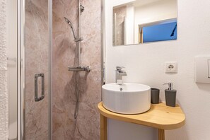 A bathroom with a glass-enclosed shower, a white sink with a wooden countertop, and a mirror above the sink. - Apartment 'Bergwelt A1' with Mountain View, Balcony and Wi-Fi (Niederau)