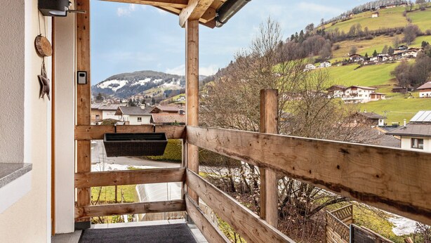 Ein hölzerner Balkon mit Blick auf ein Dorf an einem Hang und schneebedeckte Berge.