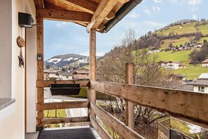 Ein hölzerner Balkon mit Blick auf ein Dorf an einem Hang und schneebedeckte Berge.