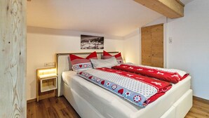 Ein Schlafzimmer mit Holzbalkendecke, einem Bett mit rot-weiß gestreifter Bettwäsche, einem Nachttisch mit Lampe und einem Wandbild.