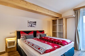 Un dormitorio con techo de madera, cama con ropa de cama roja y blanca, mesita de noche y ventana con cortinas.