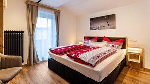A bedroom with a bed, a chair, a radiator, a window with curtains, a wall-mounted picture, and a bedside table. - Apartment 'Bergwelt A2' with Mountain View, Balcony and Wi-Fi (Niederau)