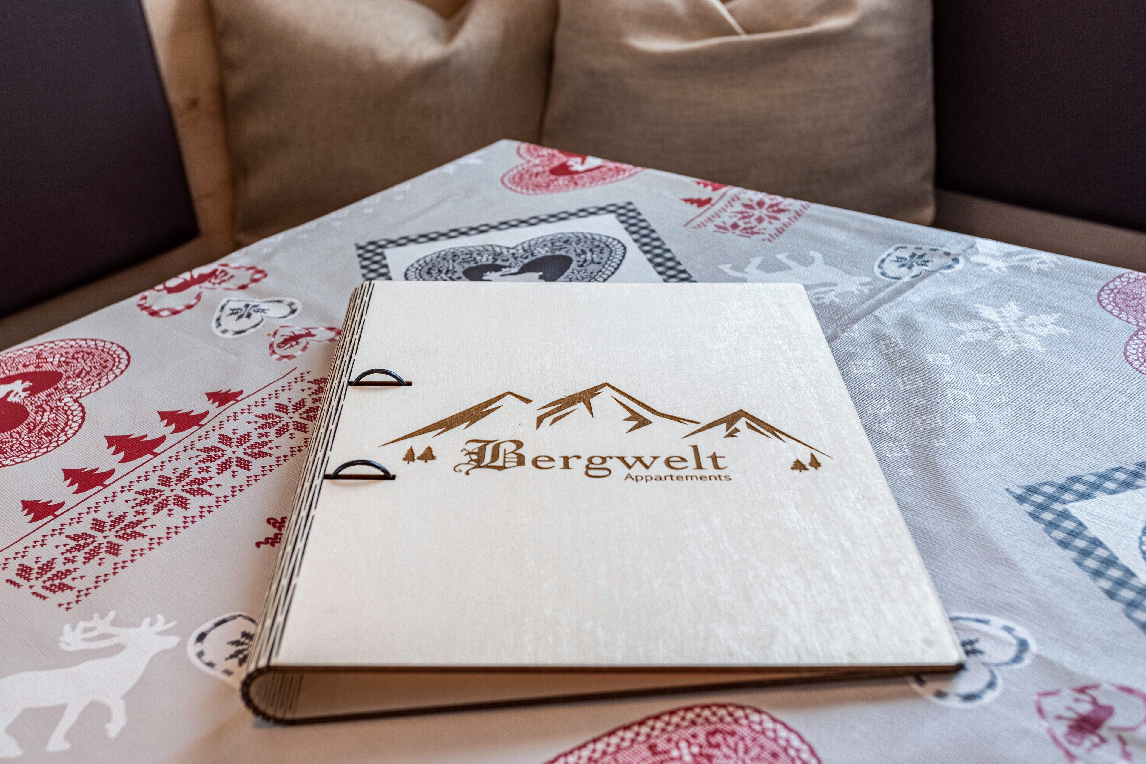 Een boek met de titel 'Bergwelt Apartments' op een tafel met een tafelkleed met dessin.