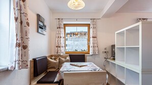 Ein gemütliches Zimmer mit Bett, kleinem Tisch, Fenster mit Vorhängen, Bücherregal und Pendelleuchte.
