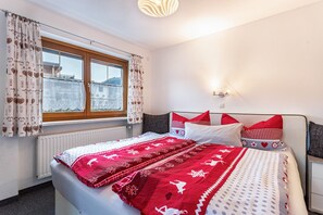 A bedroom with a bed, a window, a radiator, and a wall-mounted light fixture.