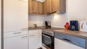 Eine kleine Küche mit Holzausstattung, einem eingebauten Ofen, einer Spülmaschine und einer Kaffeemaschine.