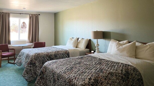 A hotel room with two beds, a desk, a chair, and a window with curtains.
