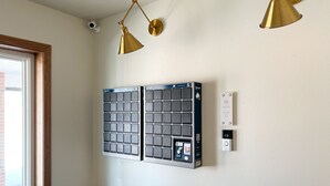 A room with a large window, a wall-mounted security camera, two wall-mounted lights, and a wall-mounted intercom system.