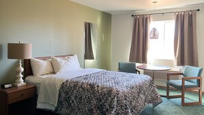A hotel room with a bed, bedside table, lamp, chair, and a small table with a chair.