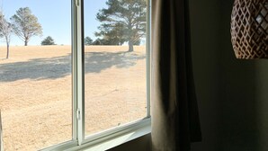 Una finestra amb vista a un camp sec i arbres.