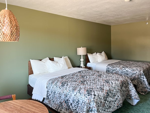 A hotel room with two beds, a wooden chair, a woven light fixture, and a bedside table with a lamp.