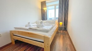 A single bed with white linens and towels, a bedside lamp, and a window with curtains.