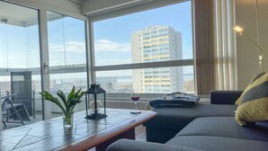 Un salón moderno con un ventanal grande, una planta en maceta, una copa de vino tinto y una lámpara.