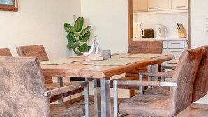 Un comedor con una mesa de madera y seis sillas, una planta en maceta y una cocina al fondo.
