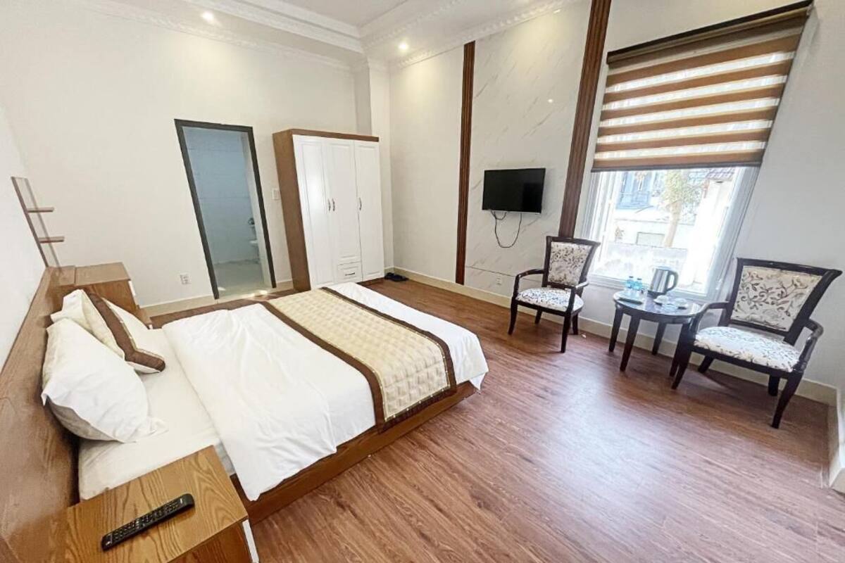 A hotel room with a bed, two chairs, a small table, a TV, and a window with blinds.