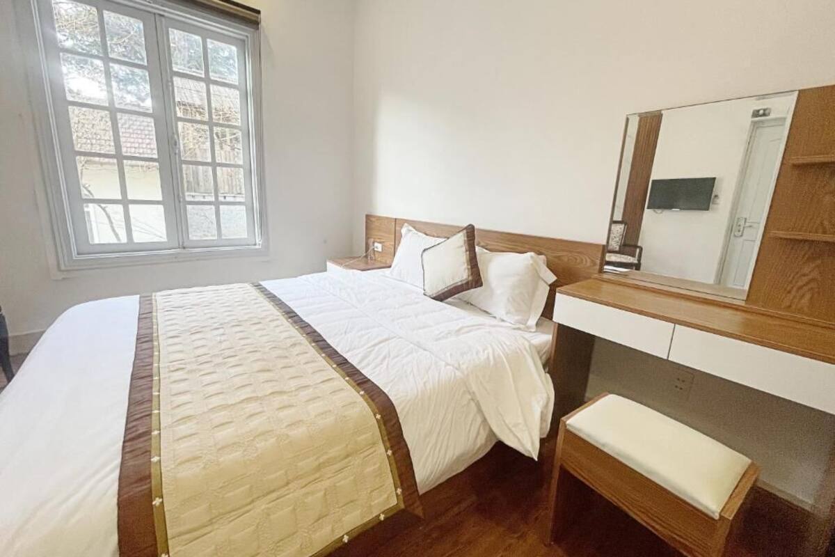 A neatly arranged bedroom with a bed, bedside table, bench, and a large mirror.