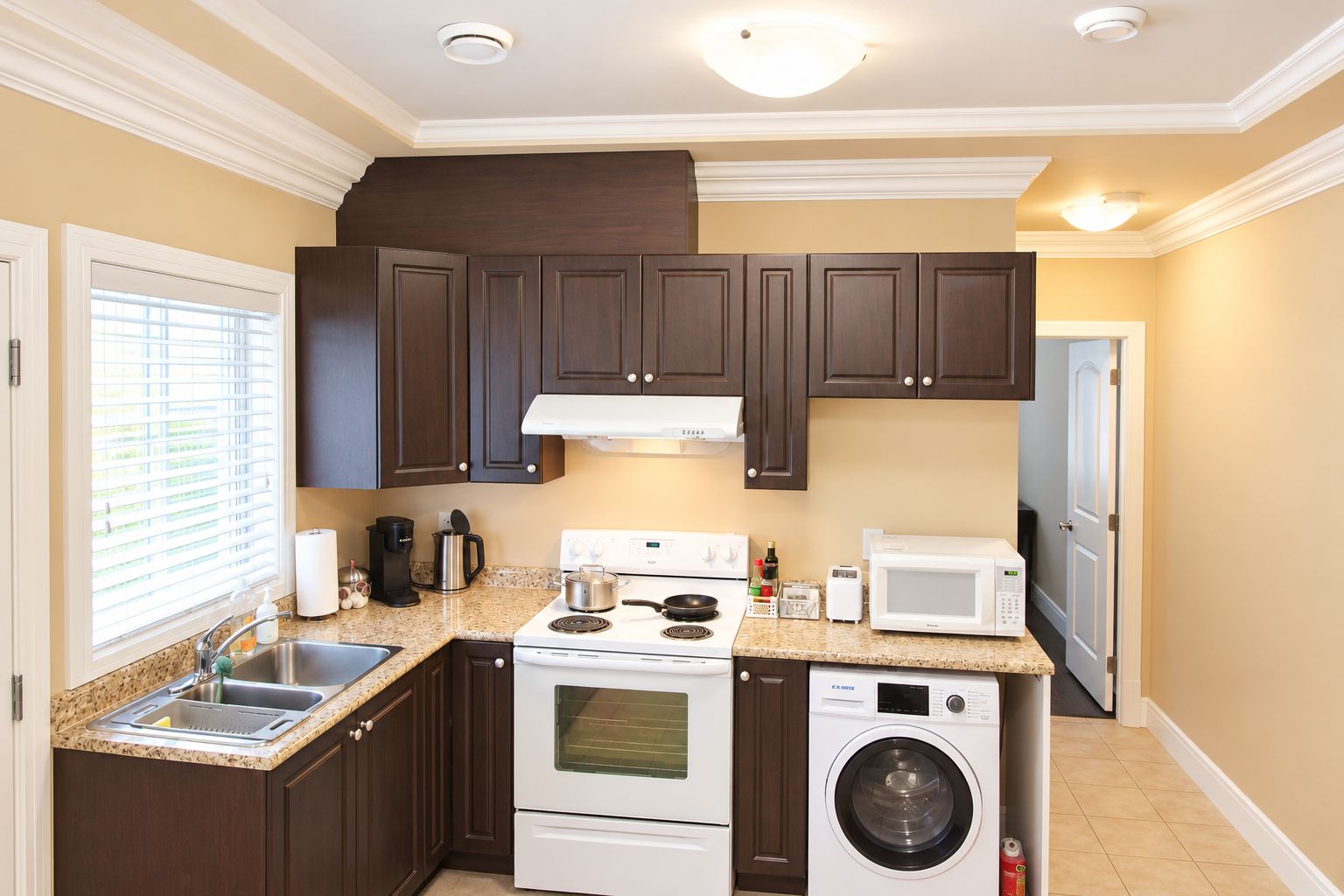 A compact kitchen with dark wooden cabinets, a white stove, a microwave, and a built-in washer and dryer.