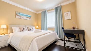 A hotel room with a bed, bedside lamps, a desk with a chair, and artwork on the walls.