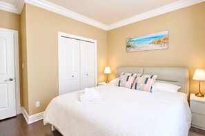 A hotel room with a large bed, two bedside tables with lamps, a painting of a beach scene, and a white door.