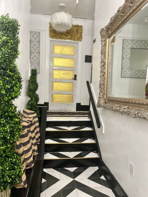 Una escalera con baldosas de diseño blanco y negro, un espejo con marco dorado y una puerta decorativa con panel dorado.