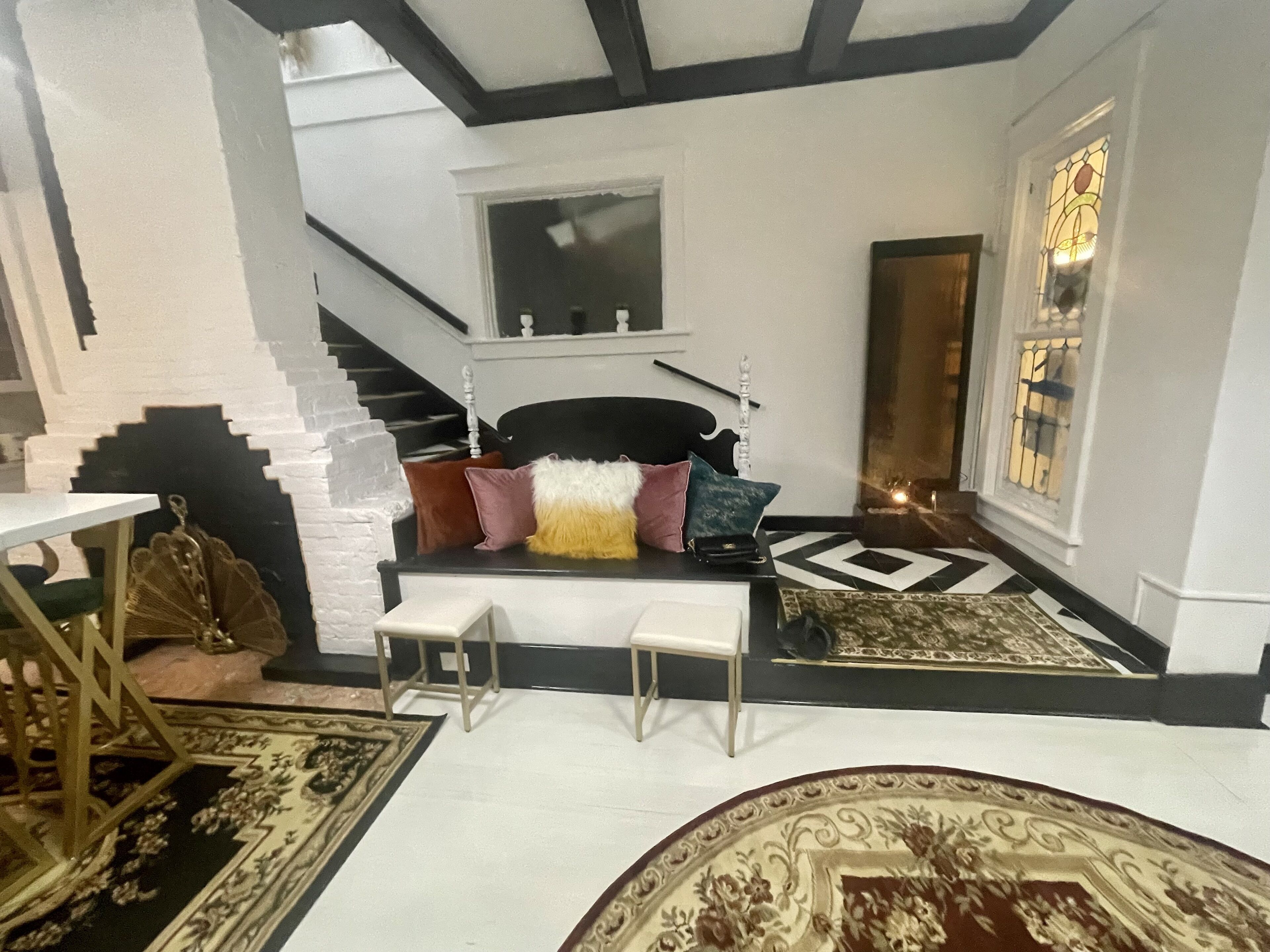 A staircase with a black railing and white walls, a black and white patterned rug, and a white bench with colorful cushions.