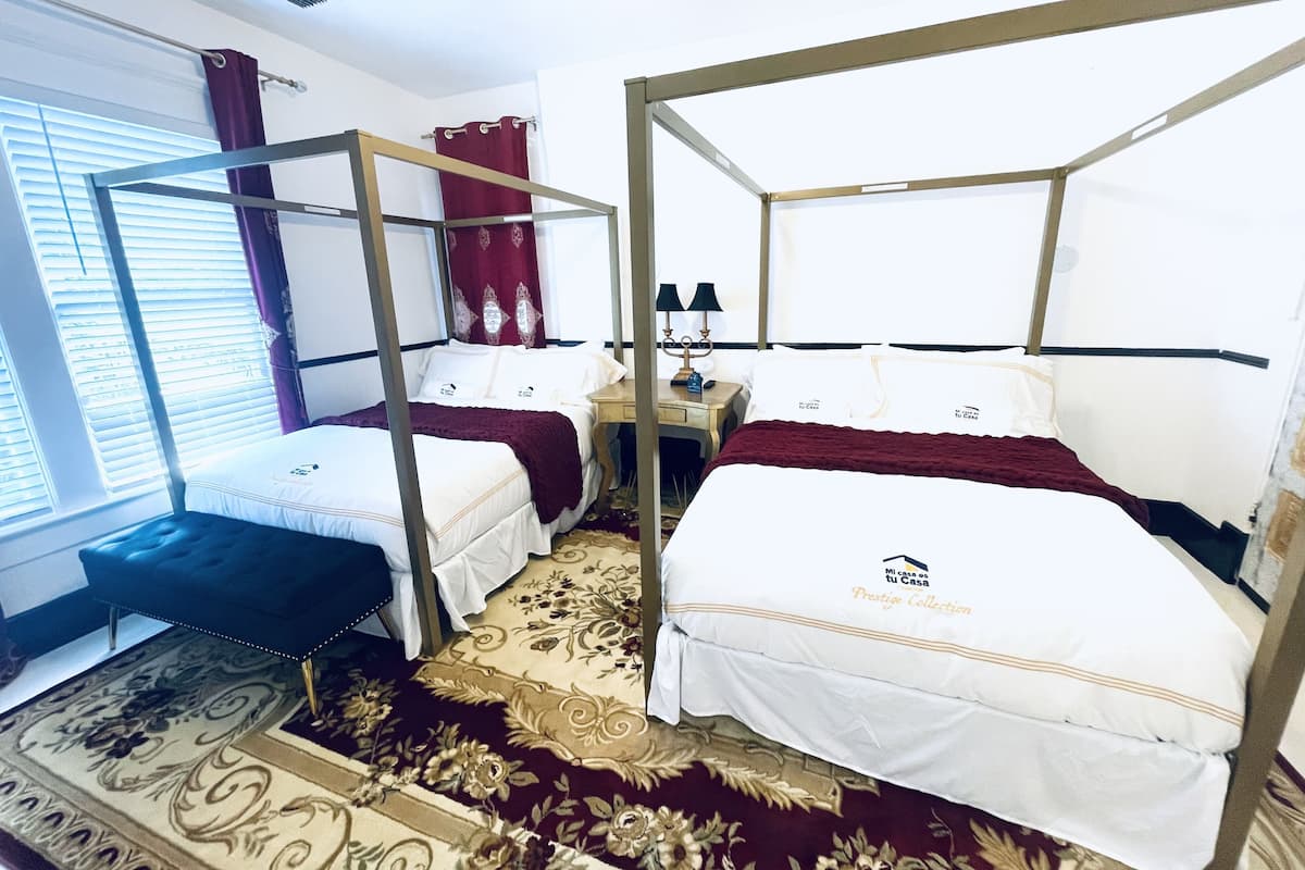 Habitación de hotel con dos camas, un escritorio y una ventana con persianas.
