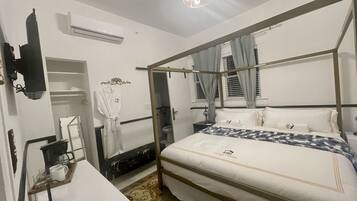 A hotel room with a four-poster bed, a bedside table with a lamp, a robe hanging on the wall, and a small seating area with a table and chairs.