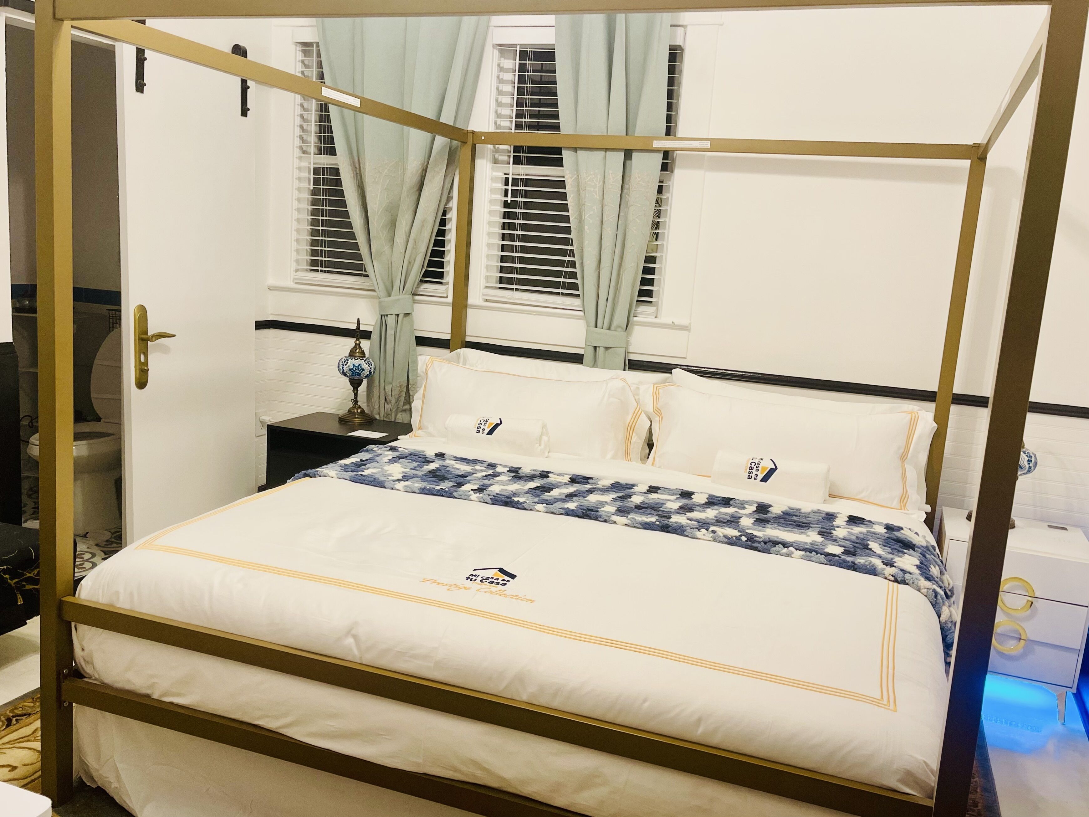 A four-poster bed with white bedding and a blue and white patterned throw.