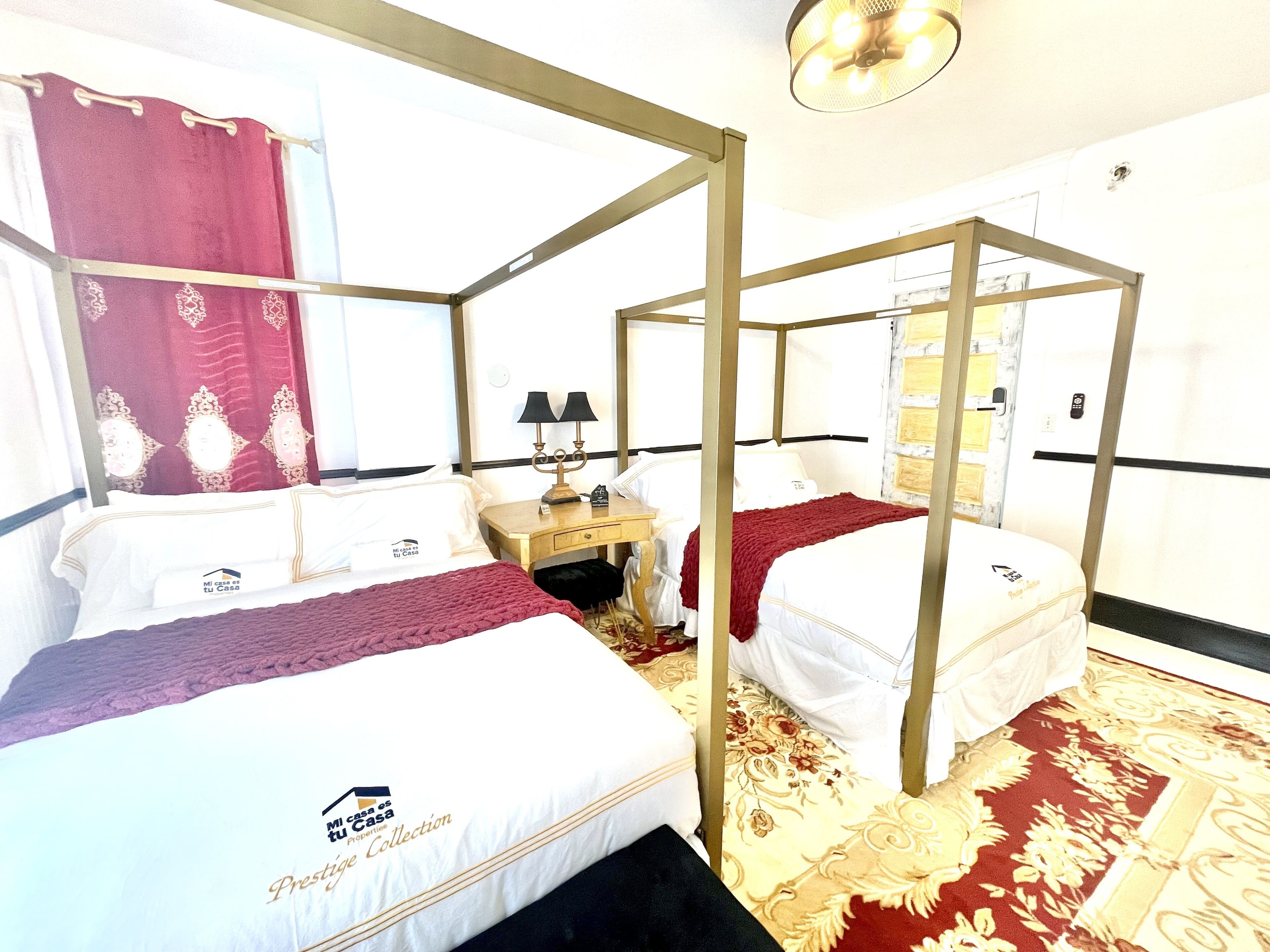 Une chambre avec un lit à baldaquin aux couleurs rouge et blanc, une table de chevet avec une lampe et un tapis à motifs.