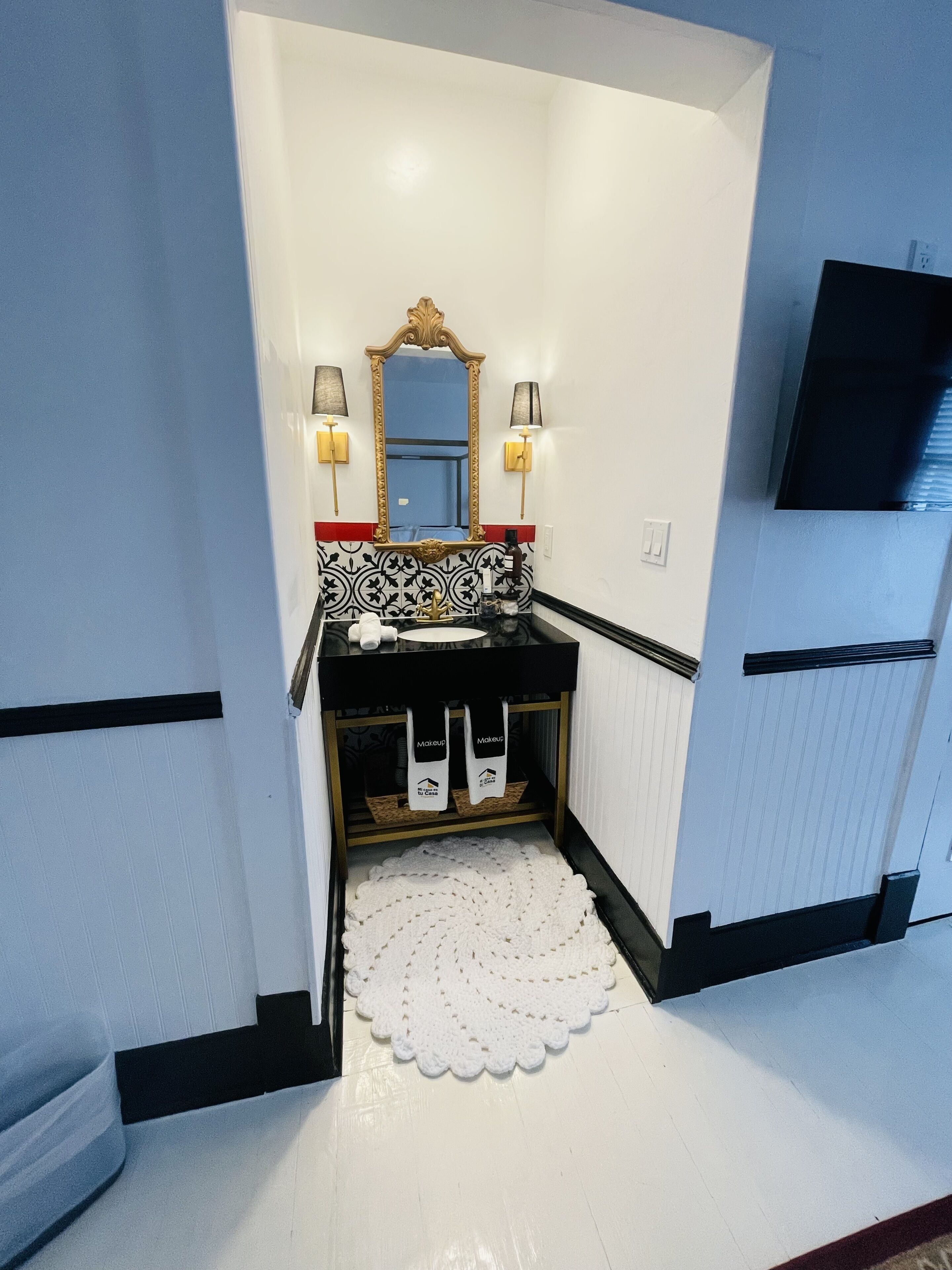 Un bagno con un mobile lavabo bianco e nero, un grande specchio, due lampade a parete e un tappetino bianco.