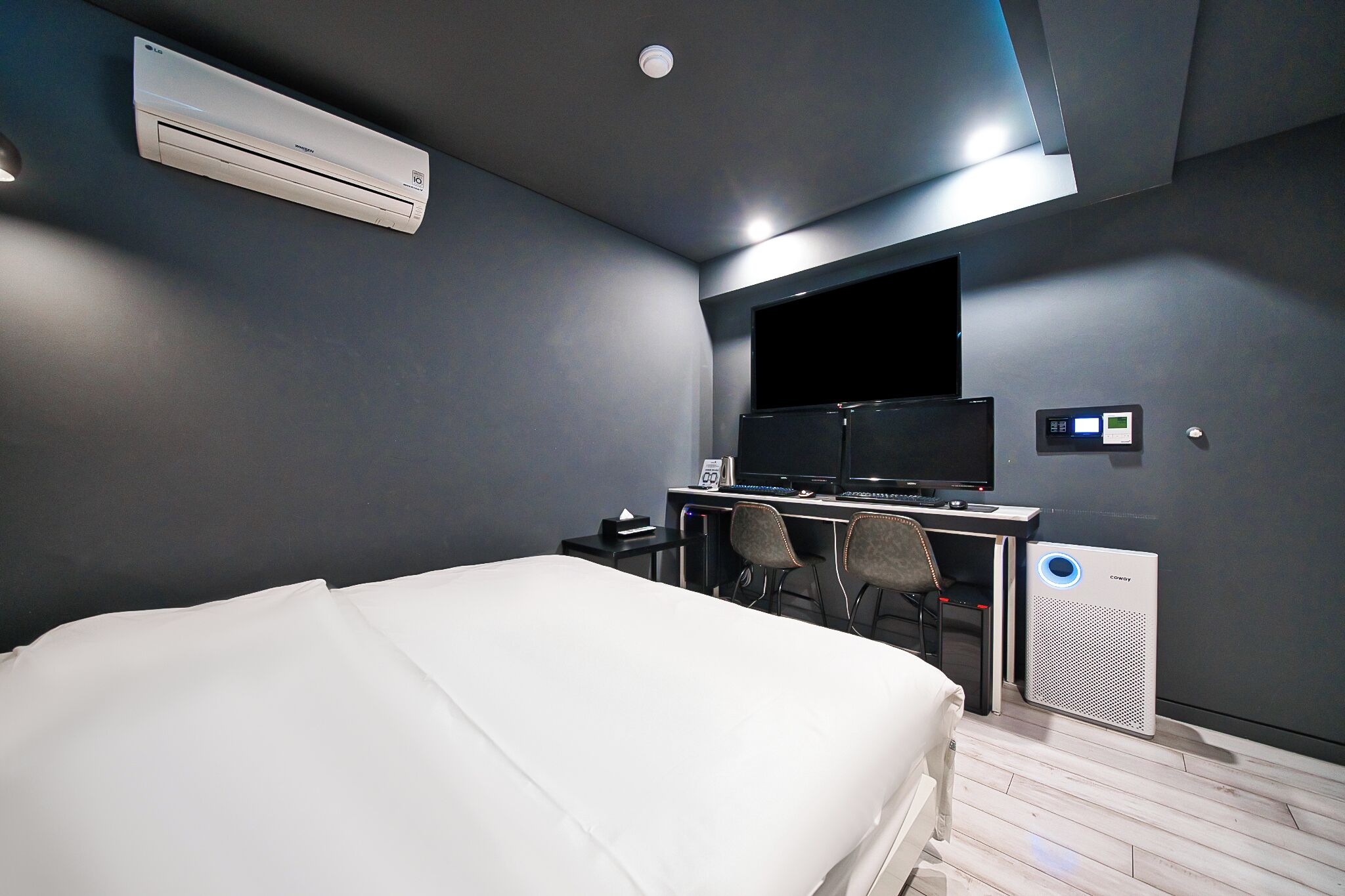 Una habitación de hotel moderna con una cama, un escritorio con una computadora y un televisor de pantalla plana, un aire acondicionado de pared y un calefactor portátil.