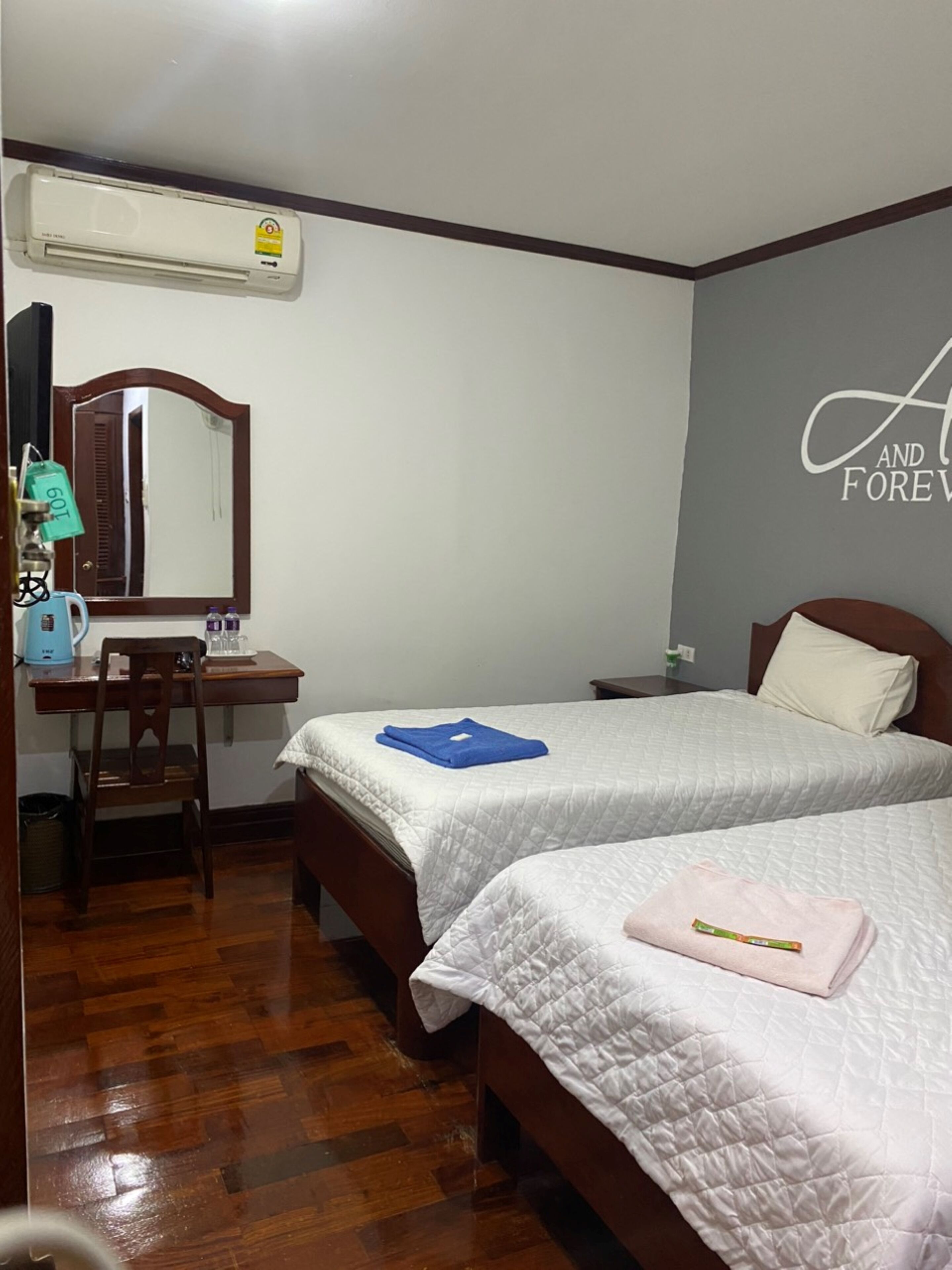 A hotel room with two beds, a desk, a chair, an air conditioner, and a mirror.