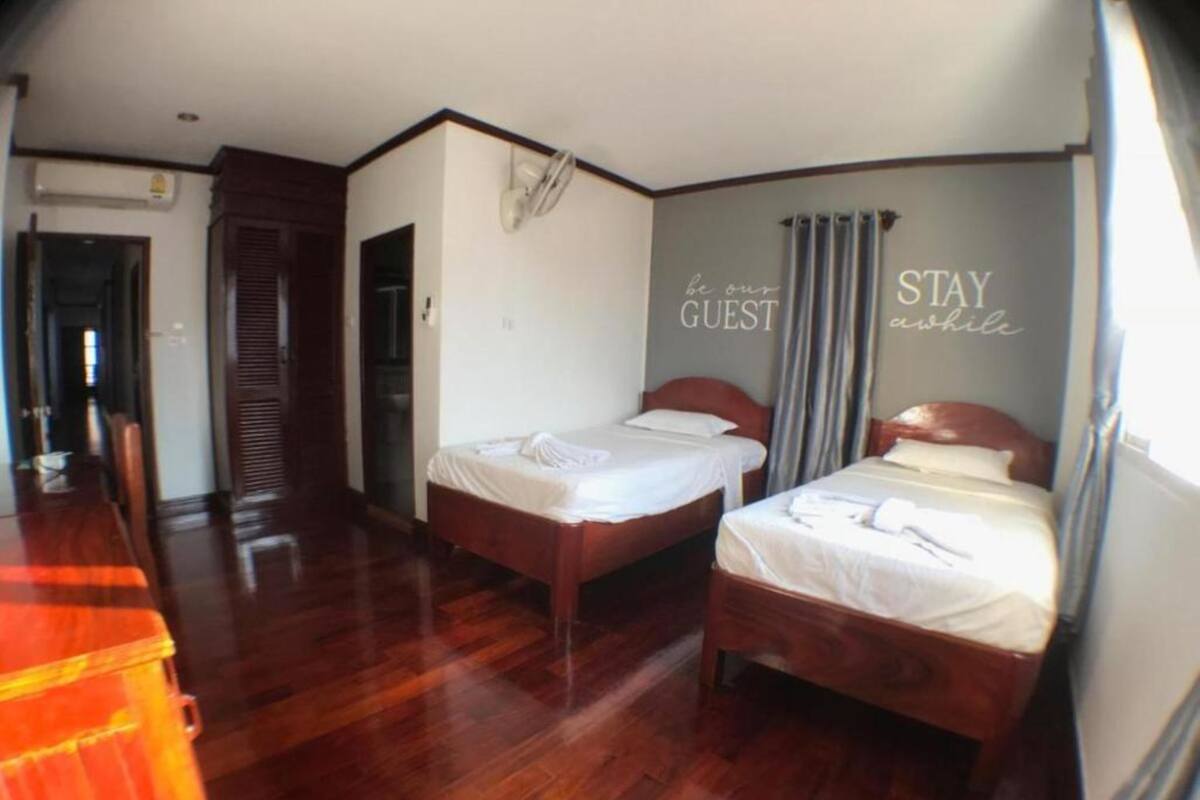 A hotel room with two wooden beds, a wooden dresser, and a wall with the text "be our guest" and "STAY while".